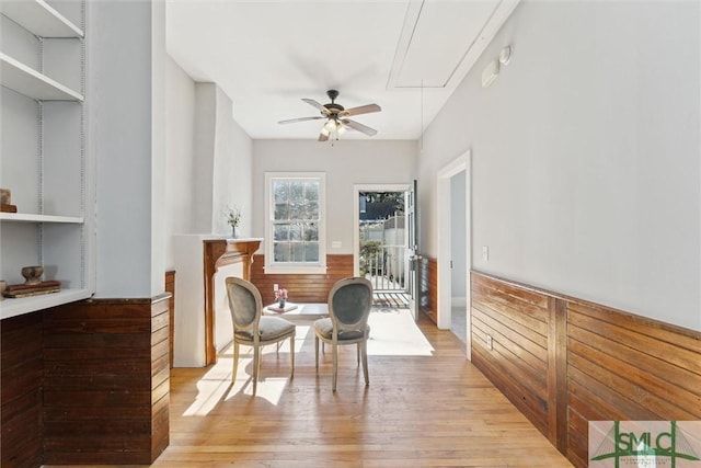 living area with wooden walls, ceiling fan, and light wood-type flooring