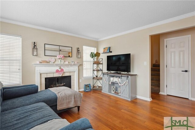 living room featuring a tiled fireplace, wood-type flooring, ornamental molding, and a textured ceiling