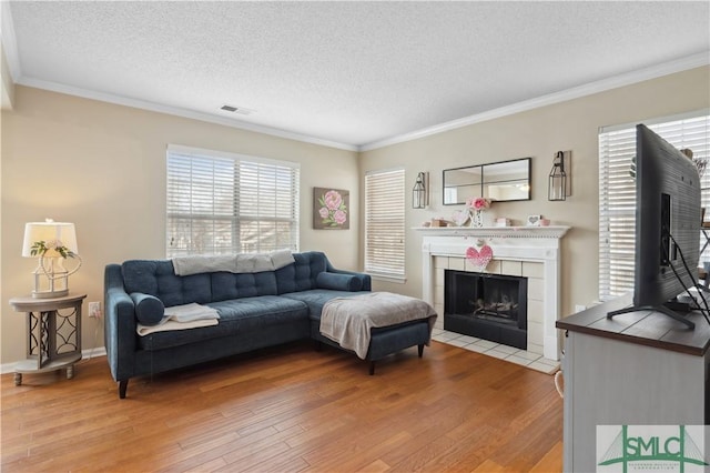 living room featuring a tiled fireplace, crown molding, and light hardwood / wood-style floors