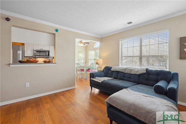 living room featuring ceiling fan, ornamental molding, a textured ceiling, and light wood-type flooring