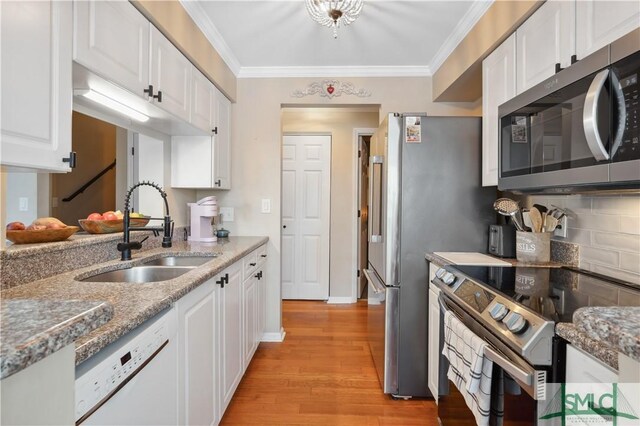 kitchen with sink, stainless steel appliances, ornamental molding, light stone countertops, and white cabinets