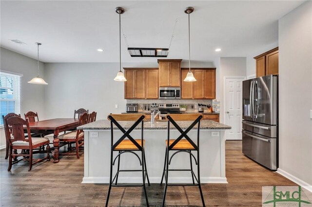 kitchen with stainless steel appliances, hanging light fixtures, a breakfast bar, and a center island with sink