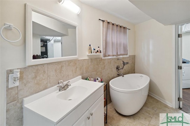 bathroom with washer / dryer, tile walls, a tub to relax in, vanity, and tile patterned floors