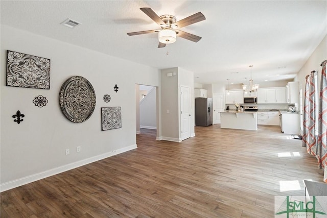 unfurnished living room with ceiling fan with notable chandelier and light wood-type flooring