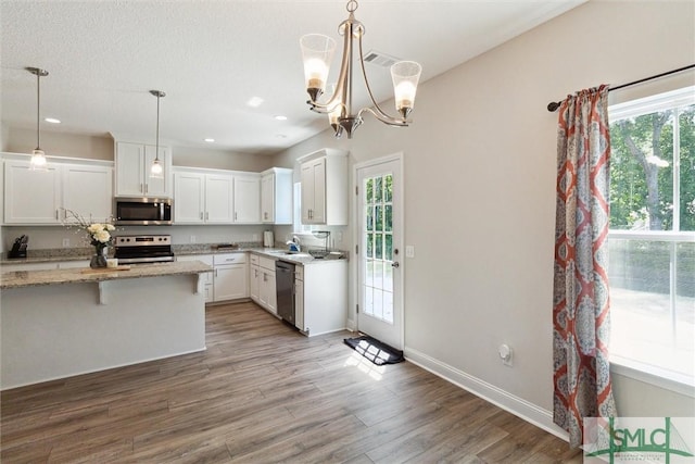 kitchen with white cabinetry, appliances with stainless steel finishes, decorative light fixtures, and hardwood / wood-style flooring