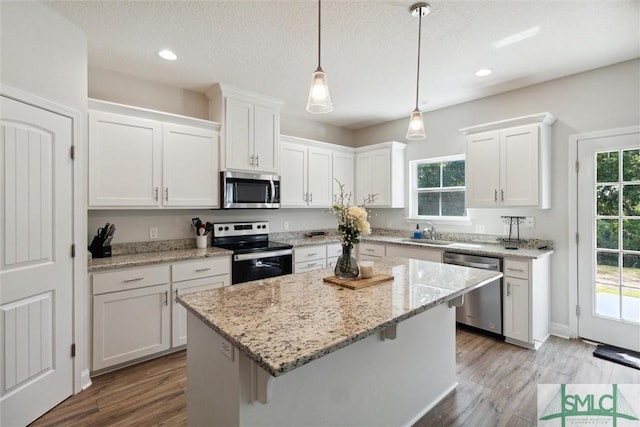 kitchen featuring sink, hanging light fixtures, stainless steel appliances, white cabinets, and a kitchen island