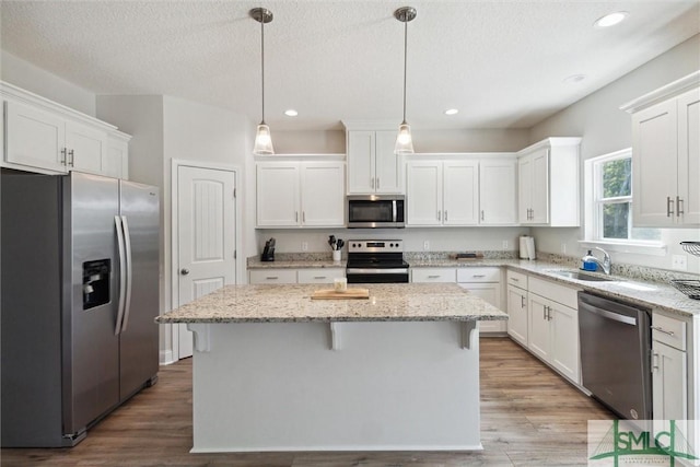 kitchen featuring pendant lighting, a kitchen island, white cabinets, and appliances with stainless steel finishes