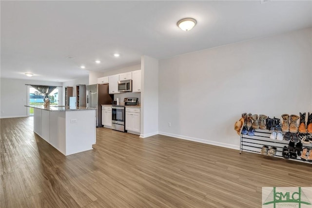 kitchen with white cabinetry, light stone counters, a center island, stainless steel appliances, and hardwood / wood-style floors