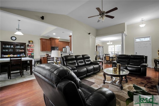 living room with ornate columns, vaulted ceiling, ceiling fan with notable chandelier, and light wood-type flooring