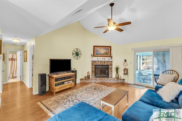 living room with light hardwood / wood-style flooring, ceiling fan, a textured ceiling, a brick fireplace, and vaulted ceiling