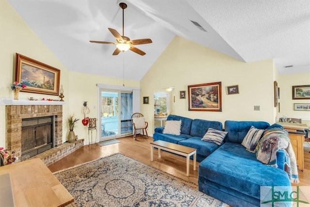 living room featuring high vaulted ceiling, a fireplace, ceiling fan, light hardwood / wood-style floors, and a textured ceiling