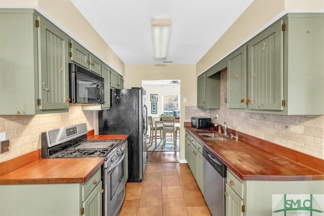 kitchen featuring light tile patterned flooring, sink, butcher block countertops, green cabinetry, and appliances with stainless steel finishes