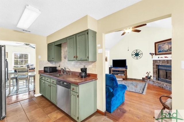 kitchen with sink, green cabinets, ceiling fan, stainless steel appliances, and a brick fireplace