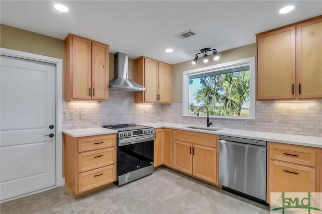 kitchen featuring wall chimney exhaust hood, light brown cabinetry, sink, appliances with stainless steel finishes, and decorative backsplash