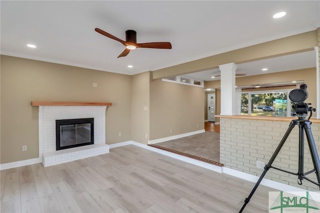 unfurnished living room featuring ceiling fan, a brick fireplace, and light wood-type flooring