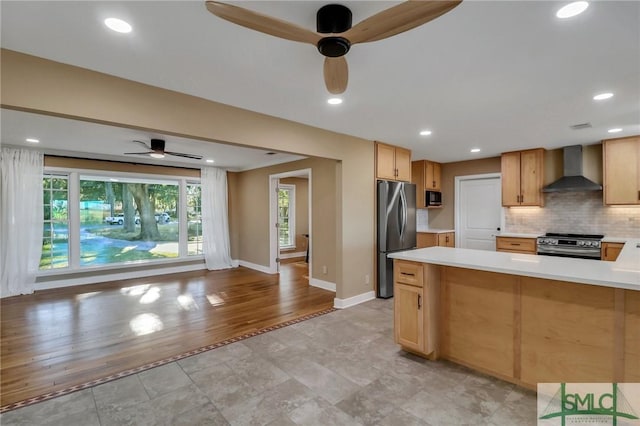 kitchen with wall chimney exhaust hood, tasteful backsplash, light hardwood / wood-style flooring, appliances with stainless steel finishes, and ceiling fan