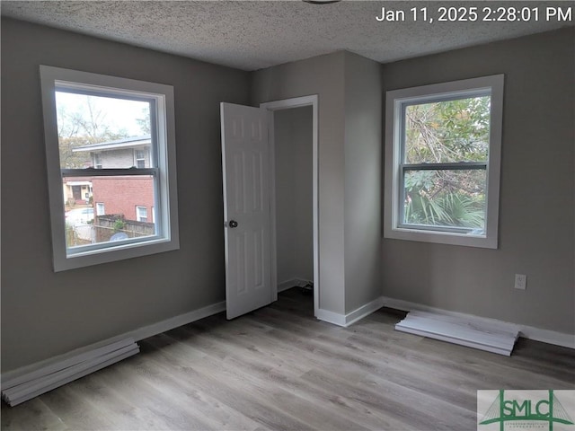 unfurnished bedroom with multiple windows, a textured ceiling, and light hardwood / wood-style floors