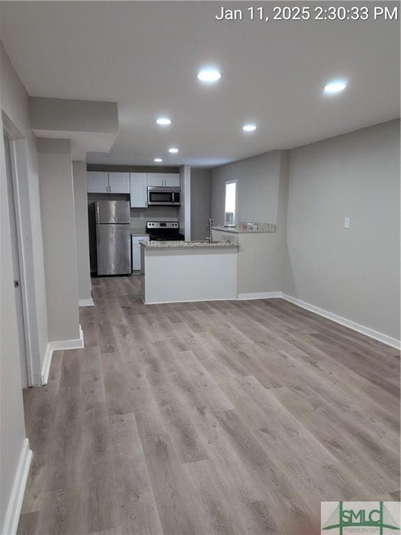 kitchen with sink, light hardwood / wood-style flooring, stainless steel appliances, light stone counters, and kitchen peninsula