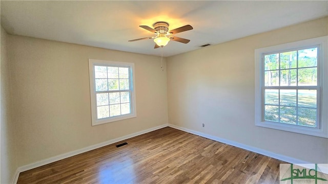 empty room featuring a wealth of natural light, visible vents, ceiling fan, and wood finished floors