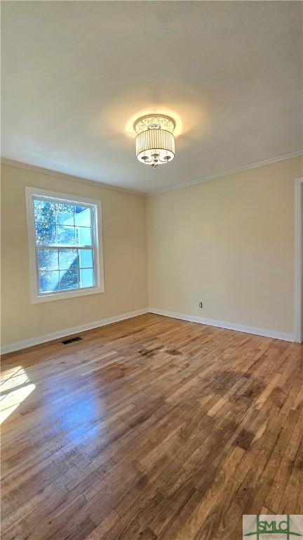 unfurnished room featuring wood finished floors, baseboards, ornamental molding, and a notable chandelier