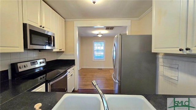 kitchen with white cabinetry, crown molding, appliances with stainless steel finishes, hardwood / wood-style floors, and backsplash