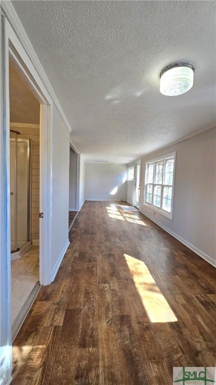 hallway with a textured ceiling, baseboards, ornamental molding, and wood finished floors