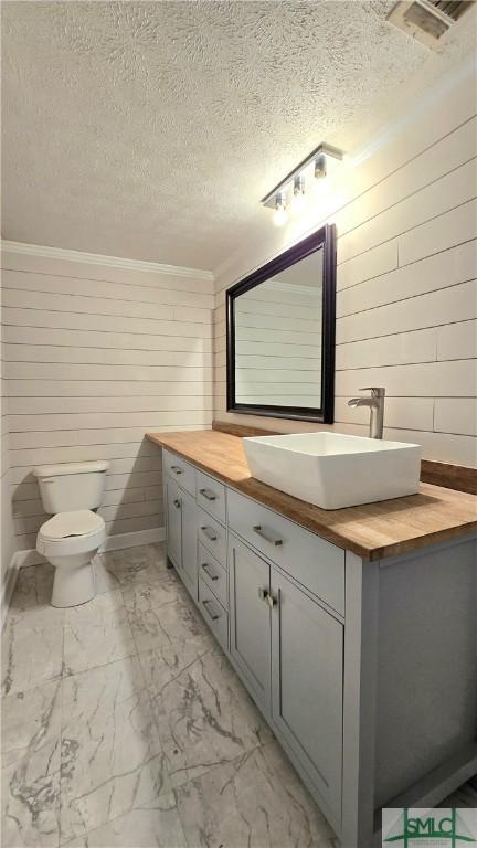 half bath featuring crown molding, a textured ceiling, vanity, toilet, and marble finish floor