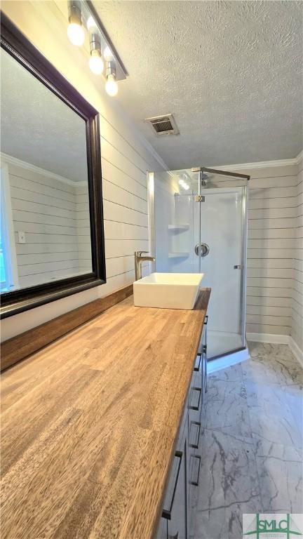 bathroom featuring vanity, wooden walls, a shower with shower door, and a textured ceiling