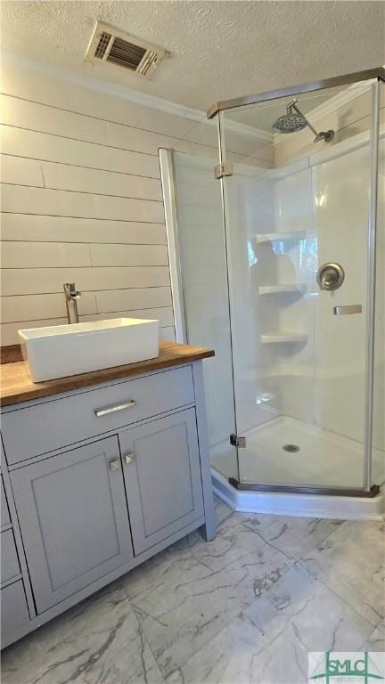 bathroom with vanity, crown molding, a shower with door, and a textured ceiling