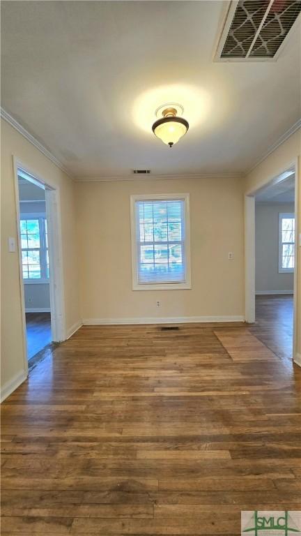 empty room featuring crown molding, dark wood-style flooring, and visible vents