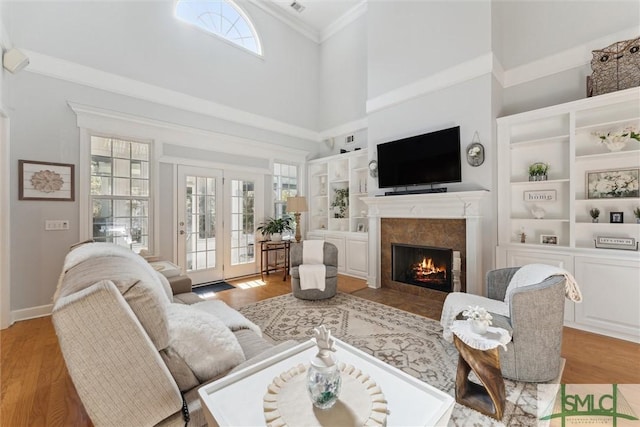 living room with crown molding, built in features, a tile fireplace, and light hardwood / wood-style flooring