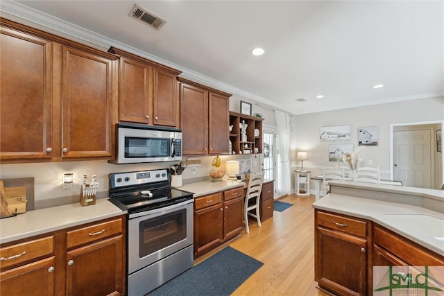 kitchen with crown molding, light hardwood / wood-style floors, and appliances with stainless steel finishes