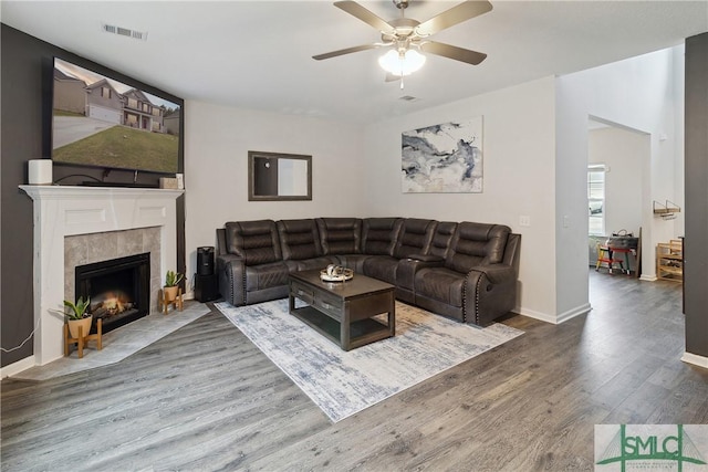 living room featuring hardwood / wood-style flooring, a tiled fireplace, and ceiling fan