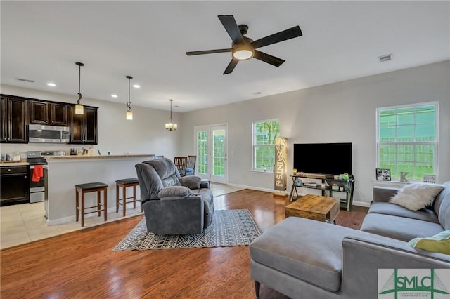 living room featuring light wood finished floors, recessed lighting, visible vents, and ceiling fan with notable chandelier