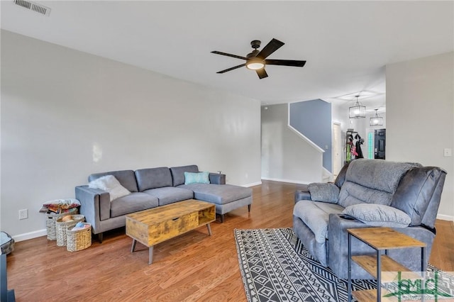 living area featuring visible vents, a ceiling fan, wood finished floors, baseboards, and stairs