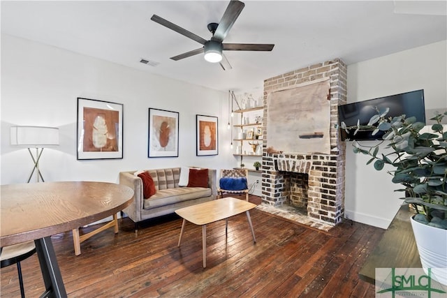 living room featuring dark wood-type flooring, ceiling fan, and a brick fireplace