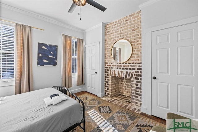 bedroom featuring ceiling fan, ornamental molding, dark hardwood / wood-style floors, and a brick fireplace