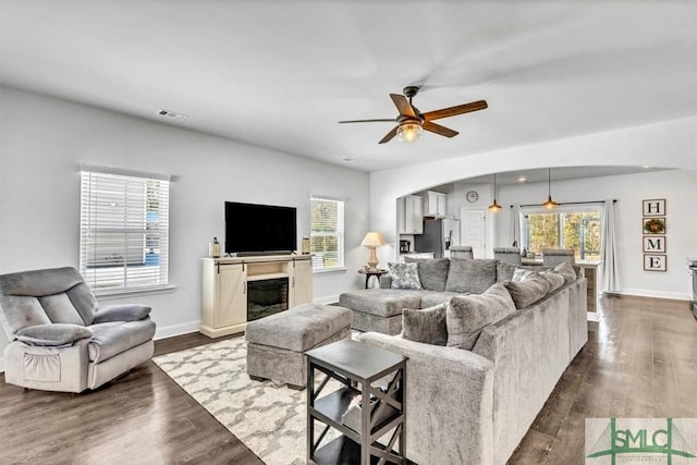 living room featuring dark wood-type flooring, ceiling fan, and plenty of natural light