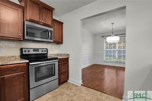 kitchen featuring pendant lighting, backsplash, ornamental molding, stainless steel appliances, and light stone countertops