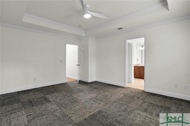 spare room featuring a raised ceiling, dark colored carpet, ceiling fan, and crown molding