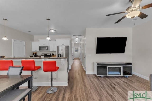 kitchen featuring hardwood / wood-style floors, white cabinets, a kitchen breakfast bar, hanging light fixtures, and stainless steel appliances