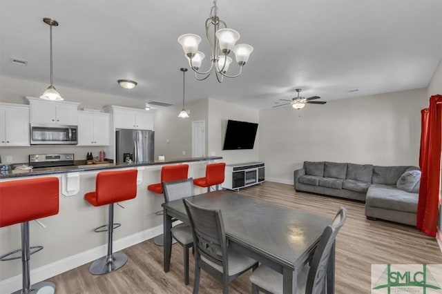 dining area with ceiling fan with notable chandelier and light hardwood / wood-style flooring