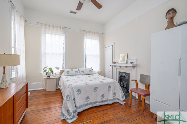 bedroom featuring a fireplace, light hardwood / wood-style flooring, a closet, and ceiling fan