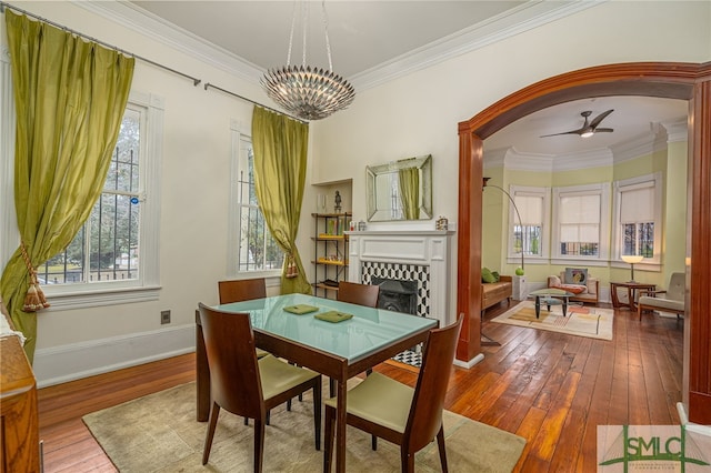 dining area featuring hardwood / wood-style flooring, ceiling fan with notable chandelier, ornamental molding, and a tile fireplace