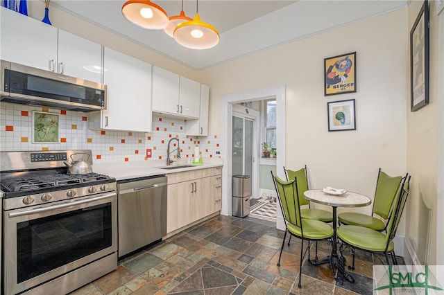 kitchen featuring sink, appliances with stainless steel finishes, hanging light fixtures, white cabinets, and decorative backsplash