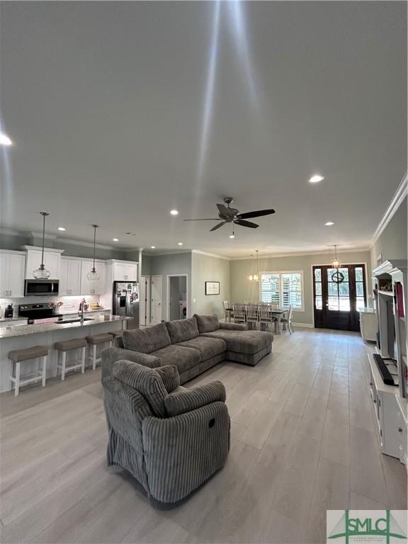 living room featuring sink, crown molding, ceiling fan, and light wood-type flooring