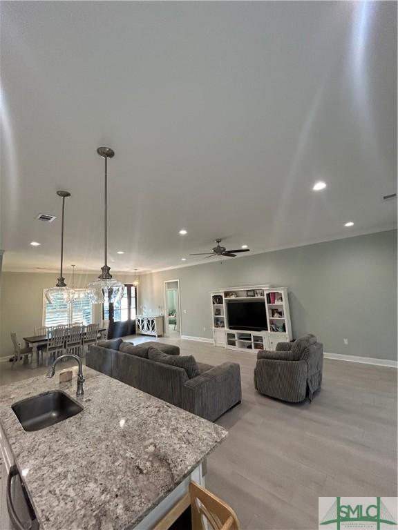 kitchen featuring sink, ceiling fan, light stone counters, light hardwood / wood-style floors, and decorative light fixtures