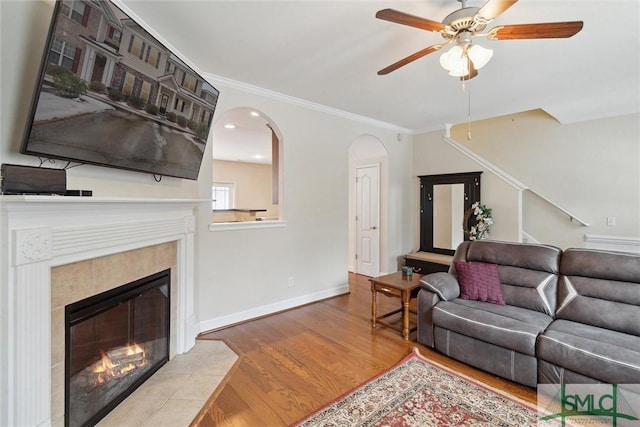 living room with a tiled fireplace, light hardwood / wood-style flooring, ornamental molding, and ceiling fan