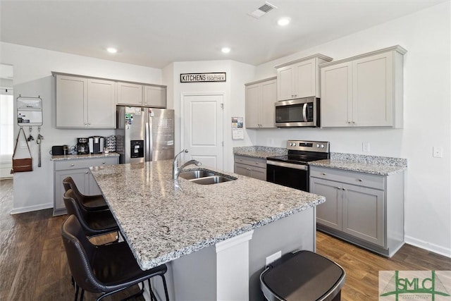 kitchen with sink, a center island with sink, stainless steel appliances, dark hardwood / wood-style floors, and a kitchen bar