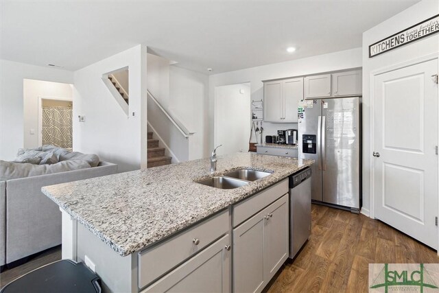 kitchen with sink, gray cabinets, stainless steel appliances, an island with sink, and dark hardwood / wood-style flooring